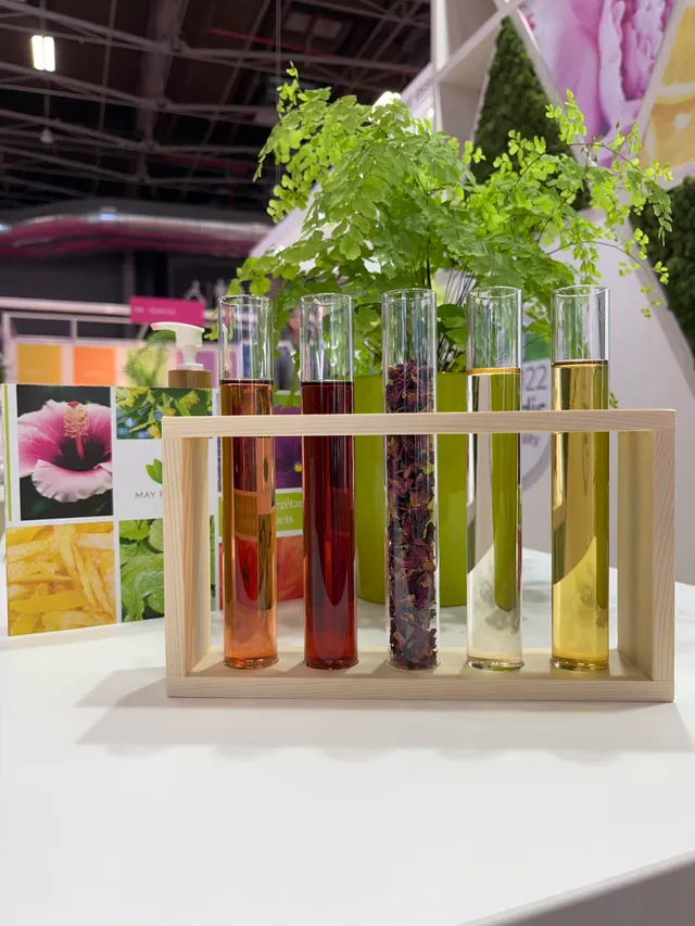 Test tubes with colored natural extracts in a wooden stand, green plants in the background, professional trade show