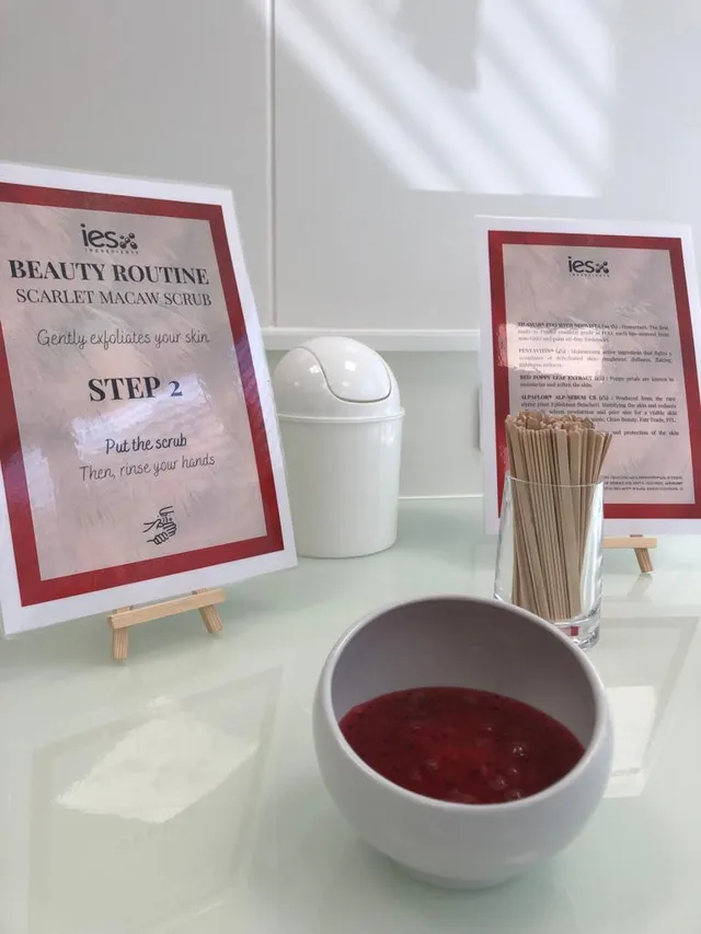 Station démonstration routine beauté IES Ingredients avec gommage macaw rouge, bâtonnets bois et instructions étape 2